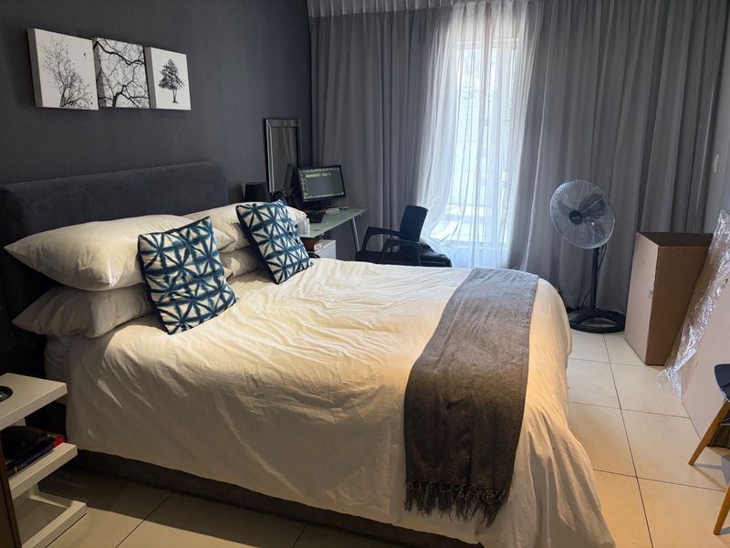 A well-lit bedroom featuring neutral tiled flooring and floor-to-ceiling curtains, providing a comfortable and functional living space.