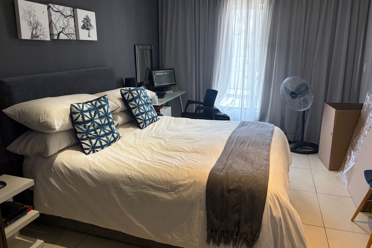 A well-lit bedroom featuring neutral tiled flooring and floor-to-ceiling curtains, providing a comfortable and functional living space.