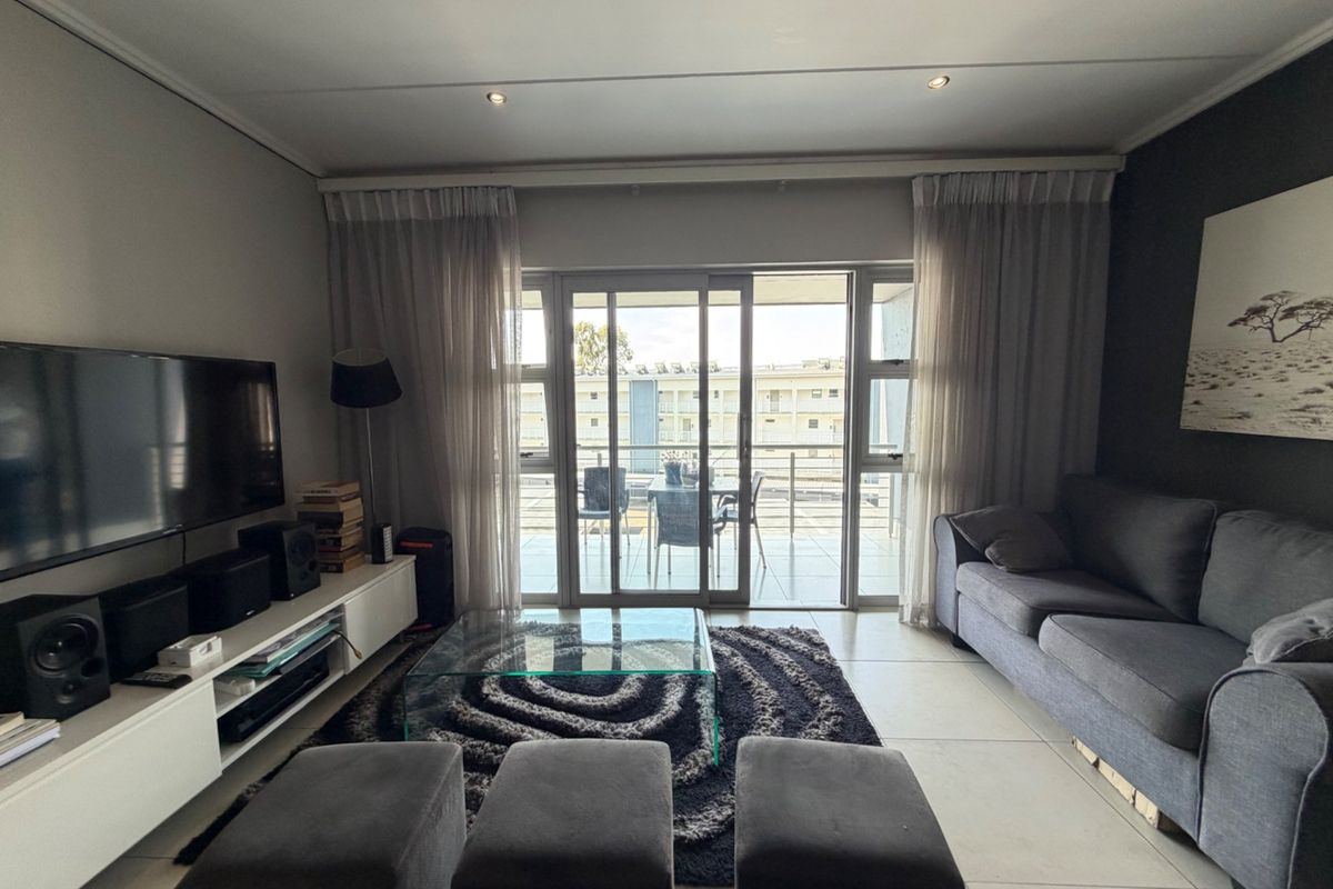 A well-maintained living room featuring large sliding glass doors that open onto a balcony, providing ample natural light and tiled flooring throughout.