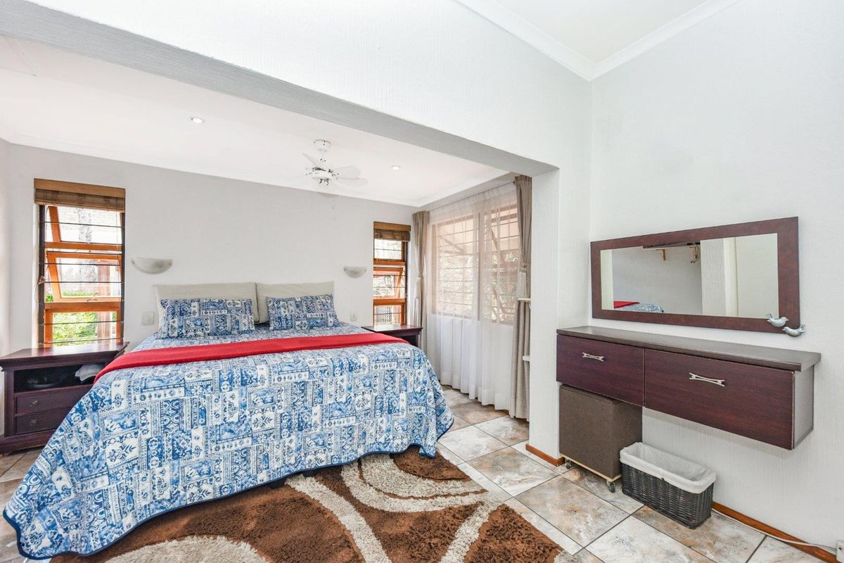 A spacious bedroom featuring tiled flooring, a ceiling fan, recessed lighting, and a built-in vanity unit with a wall-mounted mirror.