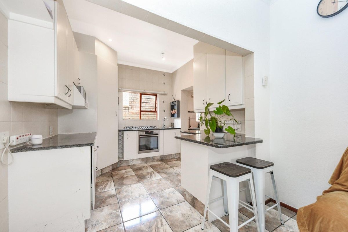 A functional kitchen featuring white cabinetry, granite countertops, a built-in oven with gas hob, and tiled flooring with an integrated breakfast nook.