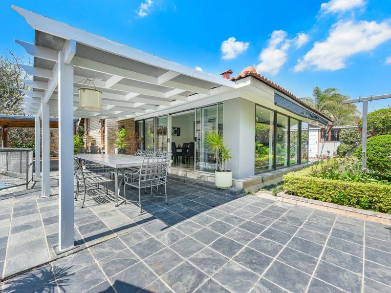A spacious covered patio featuring slate tile flooring and a pergola, seamlessly connecting to the interior through large sliding glass doors.