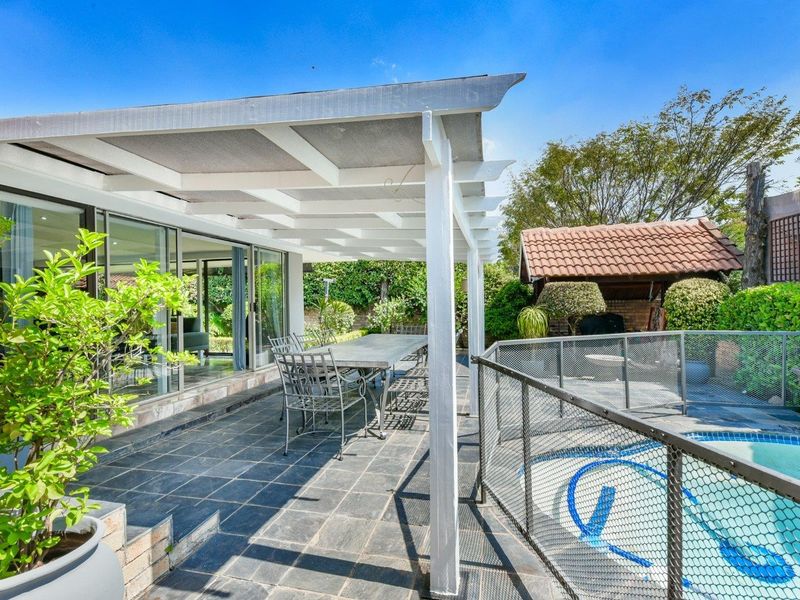 A covered outdoor patio area featuring tiled flooring, direct access to the interior via sliding glass doors, and an adjacent swimming pool with safety fencing.