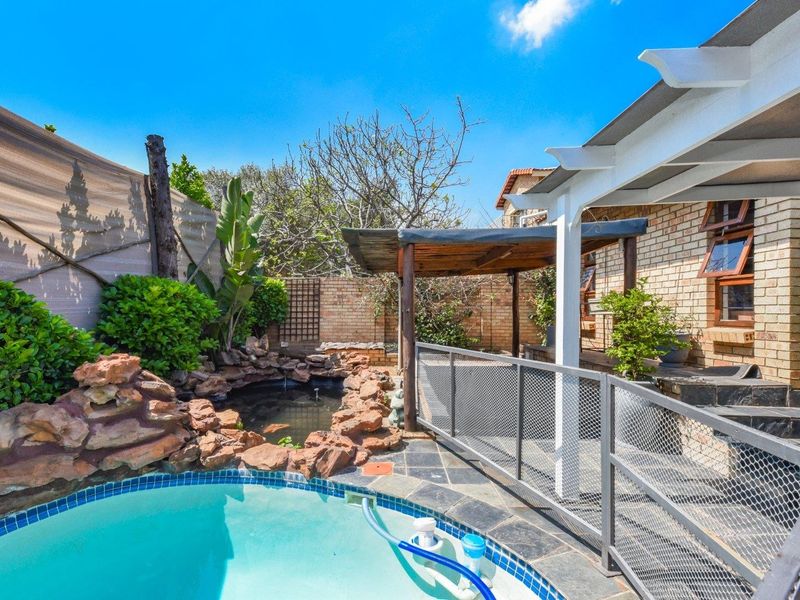 Outdoor pool area featuring a rock-lined pond, slate paving, and a covered pergola structure, providing a private and landscaped backyard entertainment space.