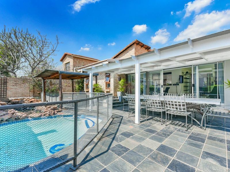 Outdoor entertainment area featuring a swimming pool with safety fencing, a covered patio with stone tiling, and direct access to the home interior.