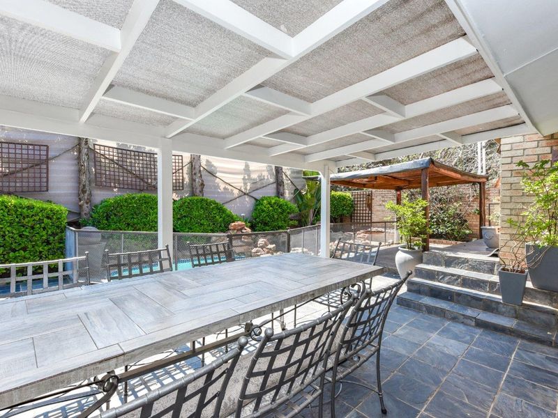 A spacious covered patio featuring slate tile flooring, brick accents, and direct access to the pool area, perfect for outdoor dining and entertaining.
