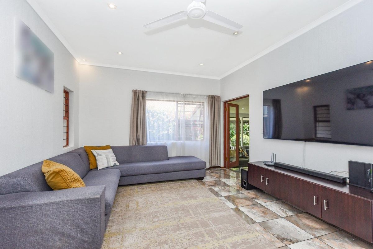 A well-maintained living room featuring tiled flooring, recessed lighting, a ceiling fan, and a glass-paneled french door leading to an adjacent space.