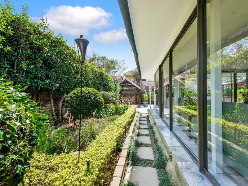 A well-maintained rear garden featuring stone paving, manicured hedging, and large sliding glass doors providing seamless indoor-outdoor flow.