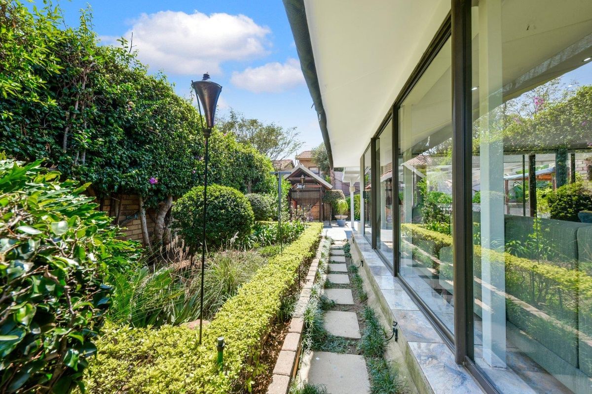 A well-maintained rear garden featuring stone paving, manicured hedging, and large sliding glass doors providing seamless indoor-outdoor flow.