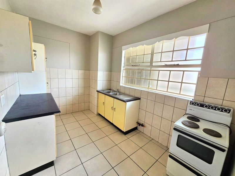 A functional, empty kitchen featuring tiled flooring, a double basin sink, built-in cabinetry, and a freestanding electric stove with a tiled splashback.