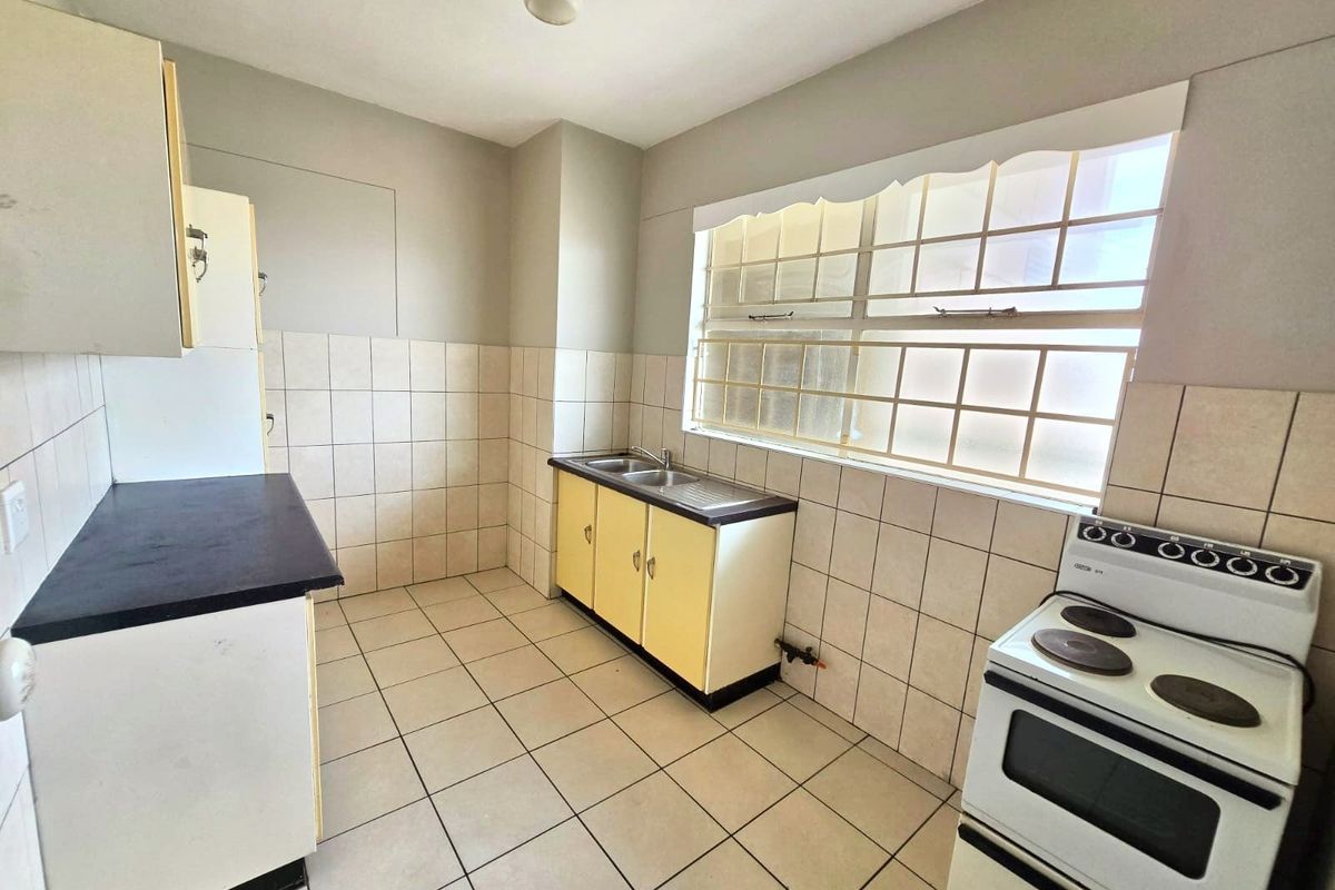 A functional, empty kitchen featuring tiled flooring, a double basin sink, built-in cabinetry, and a freestanding electric stove with a tiled splashback.
