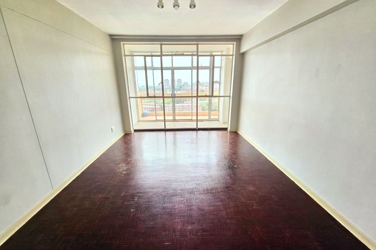 An empty living room featuring original parquet flooring, large glass sliding doors leading to a balcony, and neutral wall finishes.