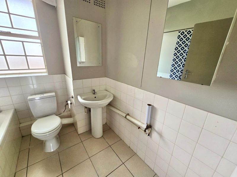 A functional bathroom featuring a pedestal basin, toilet, and tiled finishes. The space is ready for modernization and cosmetic updates.