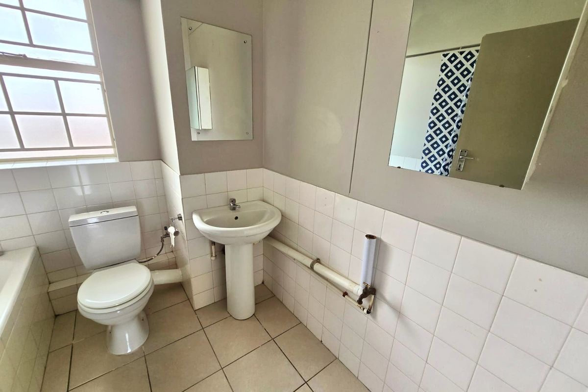 A functional bathroom featuring a pedestal basin, toilet, and tiled finishes. The space is ready for modernization and cosmetic updates.