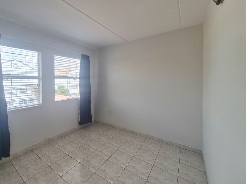 A bright, empty bedroom featuring neutral tiled flooring and windows fitted with security bars, offering a clean canvas for personalization.