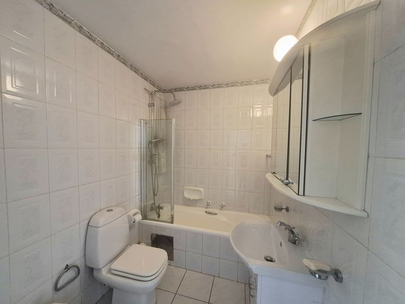 A functional bathroom featuring a bathtub with shower attachment, pedestal sink, and mirrored cabinetry, finished with classic white ceramic wall and floor tiles.
