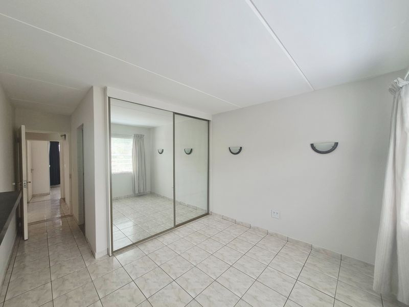 A bright, empty bedroom featuring tiled flooring, a large built-in mirrored wardrobe, and wall-mounted lighting fixtures.