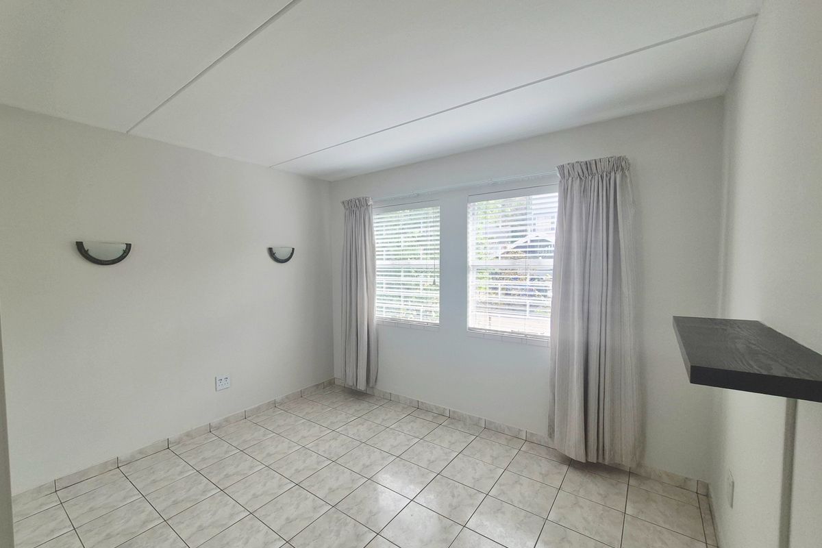 A bright, empty bedroom featuring neutral tiled flooring, wall-mounted lighting, and a built-in floating shelf, offering a clean canvas for personalization.