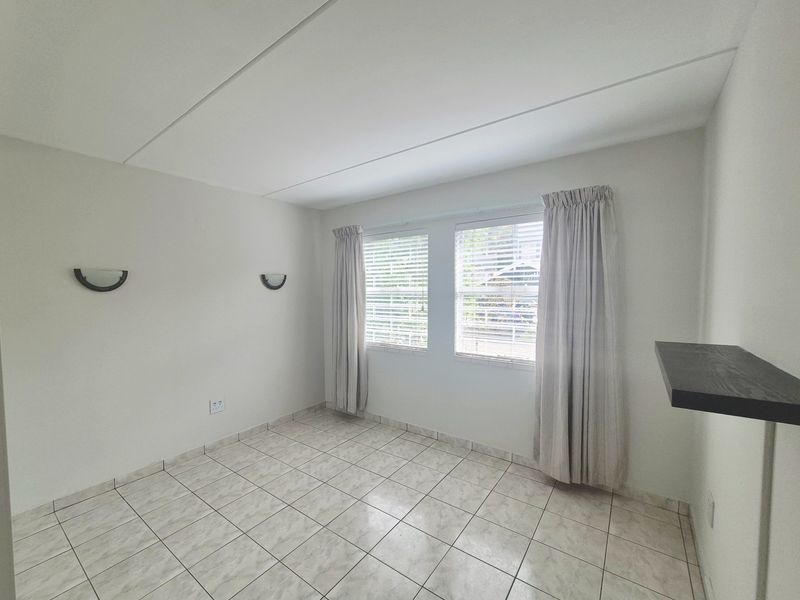 A bright, empty bedroom featuring neutral tiled flooring, wall-mounted lighting, and a built-in floating shelf, offering a clean canvas for personalization.