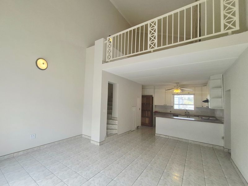 Spacious open-plan living area featuring tiled floors, a mezzanine level with a metal balustrade, and an integrated kitchen with breakfast bar.