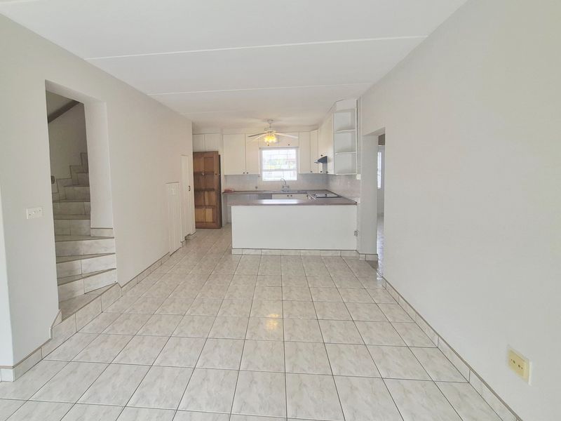 An open-plan living and kitchen area featuring tiled flooring, a functional kitchen peninsula, and an adjacent staircase.