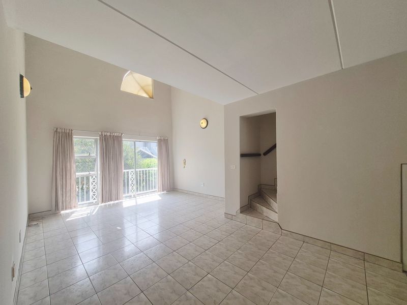 Spacious, light-filled living area featuring high vaulted ceilings, tiled flooring, and direct access to a balcony through sliding glass doors.