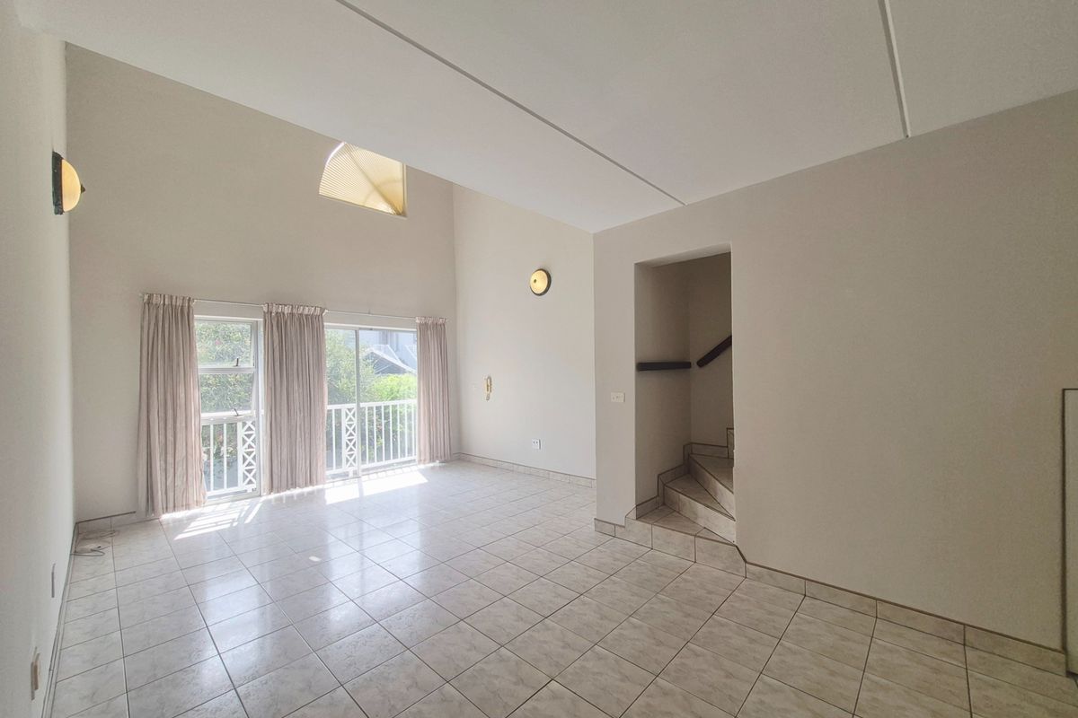 Spacious, light-filled living area featuring high vaulted ceilings, tiled flooring, and direct access to a balcony through sliding glass doors.