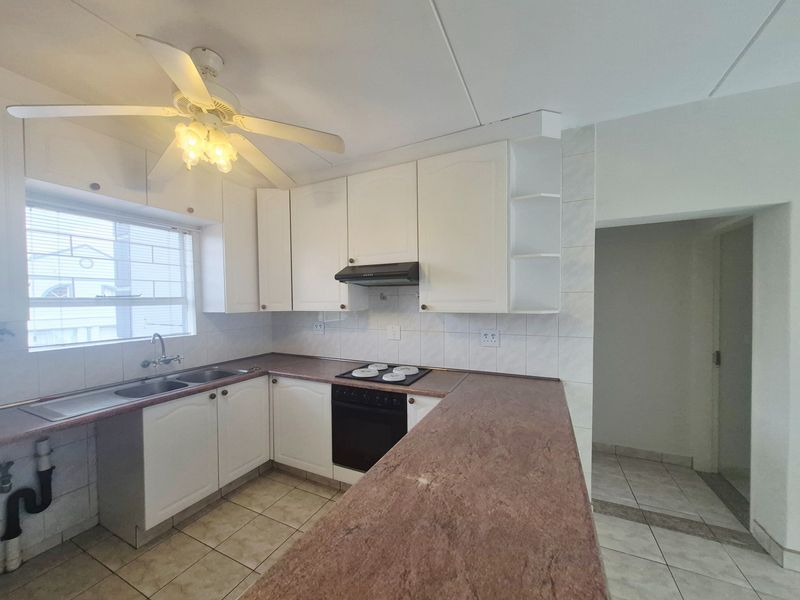 A functional kitchen featuring white cabinetry, laminate countertops, built-in oven and hob, and tiled flooring, offering a clean canvas for potential updates.