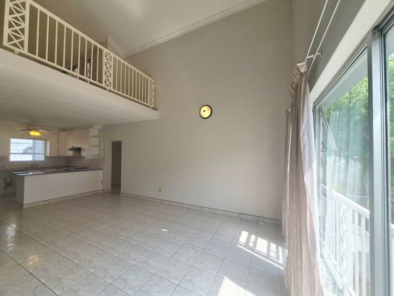 Spacious open-plan living area featuring a mezzanine level, vaulted ceilings, tiled flooring, and direct access to an outdoor space through sliding glass doors.
