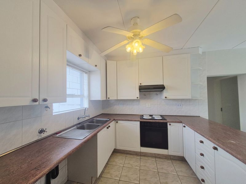 A functional kitchen featuring white cabinetry, a double basin sink, built-in oven with hob, and tiled flooring, offering a clean canvas for modern updates.