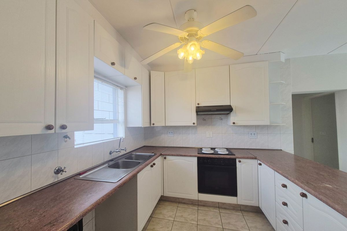 A functional kitchen featuring white cabinetry, a double basin sink, built-in oven with hob, and tiled flooring, offering a clean canvas for modern updates.