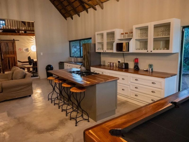Spacious open-plan kitchen and living area featuring a central island, wooden countertops, polished concrete floors, and exposed timber roof trusses.