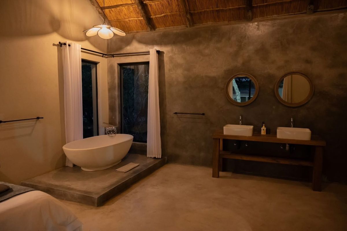 A luxurious bathroom featuring a freestanding bathtub, double vessel sinks on a wooden vanity, and a unique thatched roof ceiling with concrete finishes.