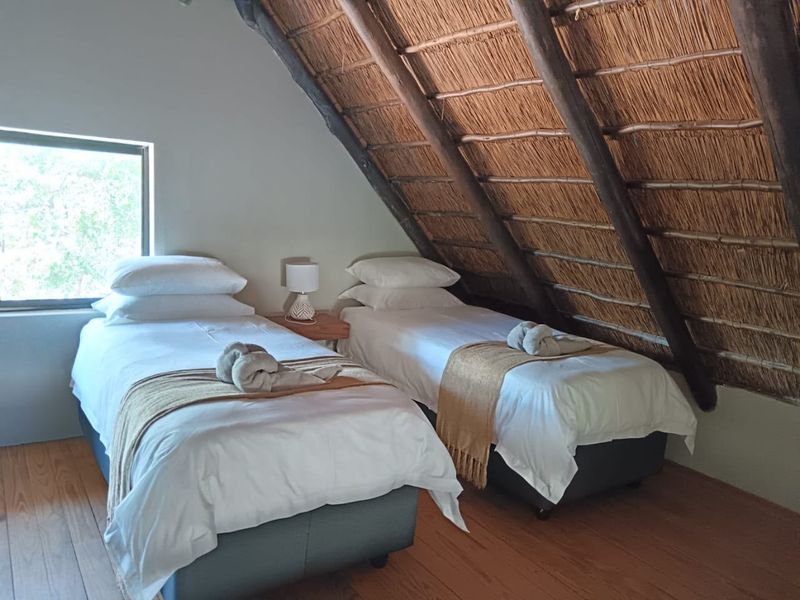 A cozy bedroom featuring a rustic exposed thatch roof with timber rafters and warm timber flooring, creating a charming and inviting atmosphere.