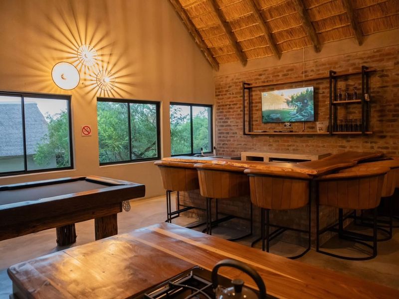A rustic bar area featuring exposed brick walls, a high thatched ceiling, concrete flooring, and a built-in bar counter with integrated shelving.
