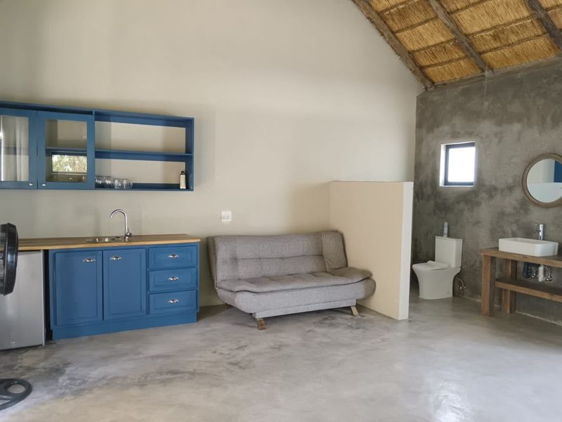 Open-plan studio space featuring a kitchenette with blue cabinetry, polished concrete flooring, a thatched roof, and an integrated bathroom area.