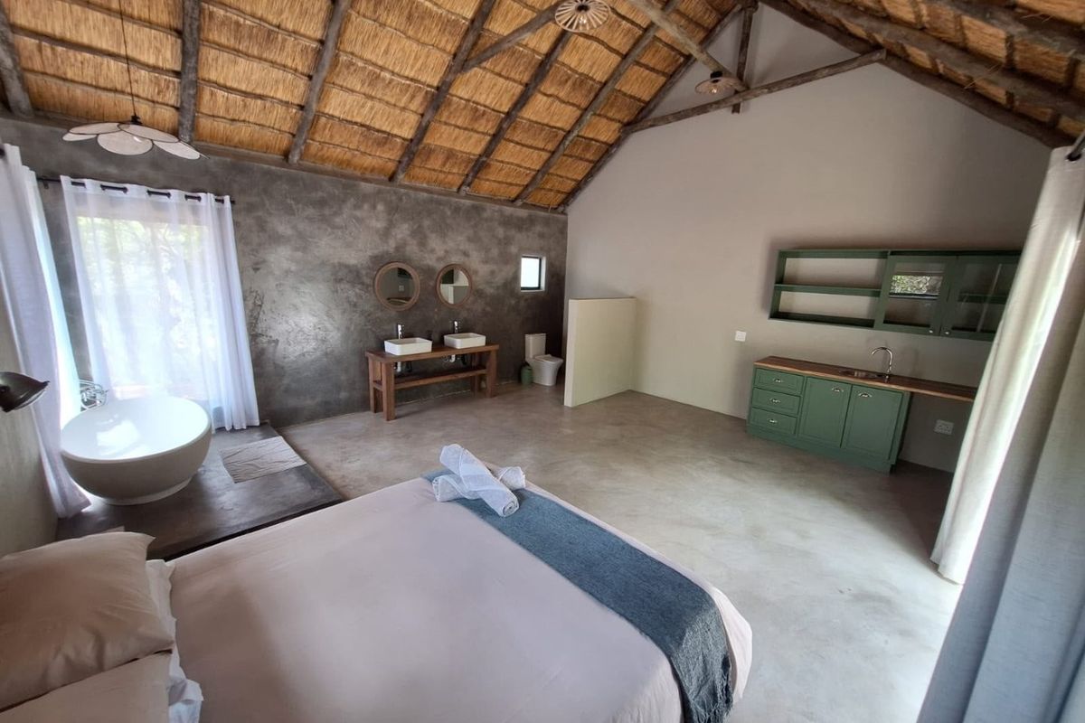 Spacious bedroom featuring a high thatched roof with exposed trusses, concrete flooring, a freestanding bathtub, double vanity, and integrated cabinetry.