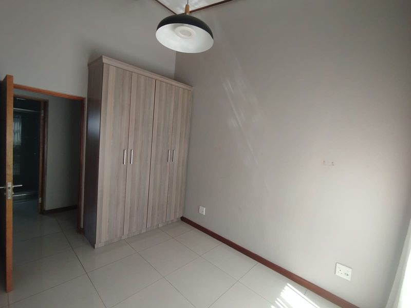 A clean, empty bedroom featuring neutral tiled flooring, a modern built-in wardrobe, and a contemporary pendant light fixture.