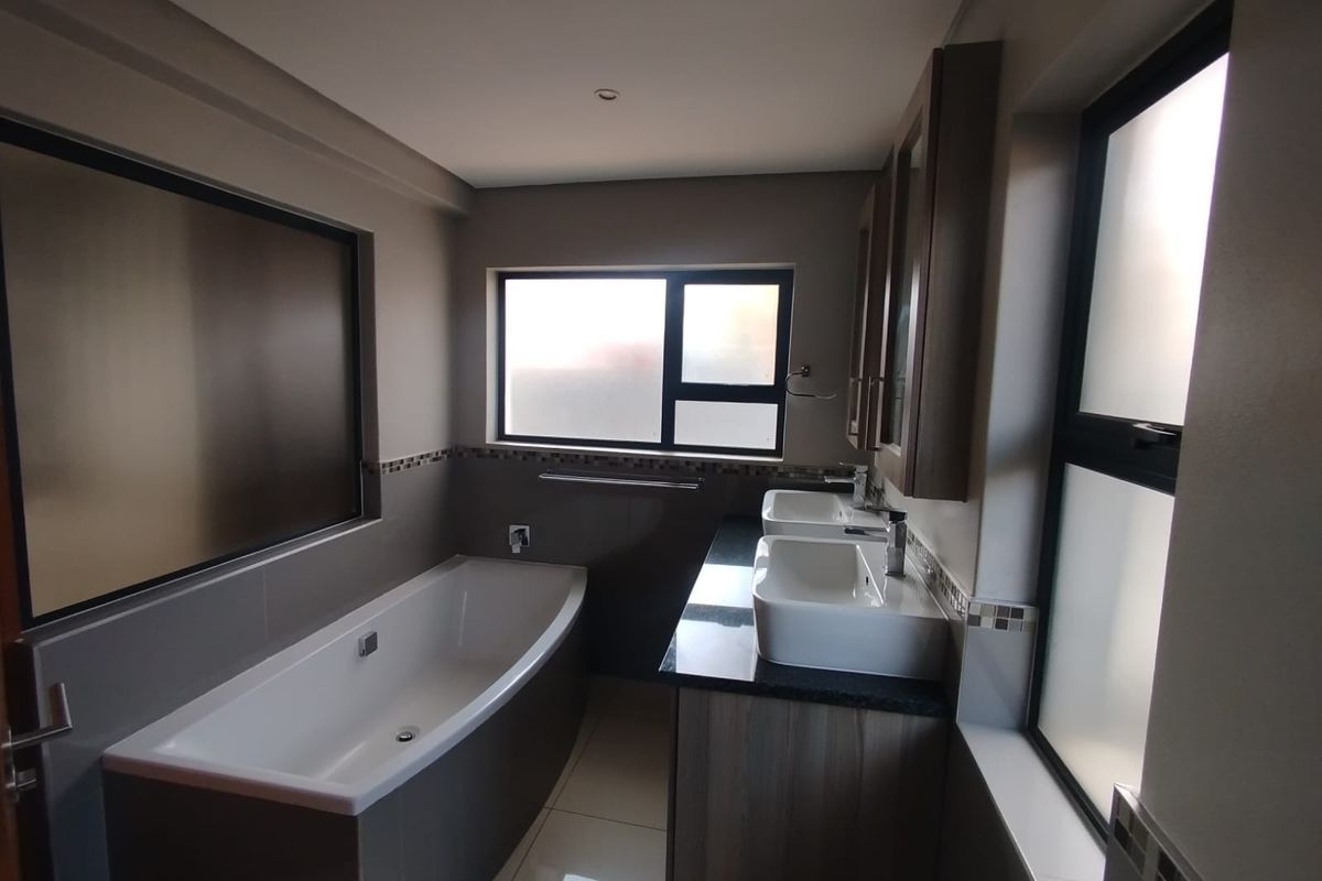 Modern bathroom featuring a built-in bathtub, double vanity with granite countertop, and tiled finishes with frosted glass windows for privacy.