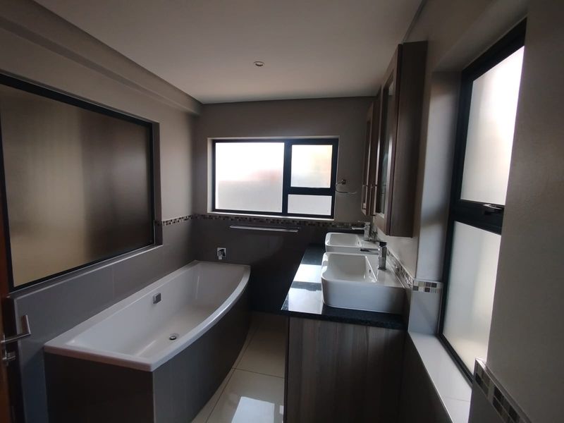 Modern bathroom featuring a built-in bathtub, double vanity with granite countertop, and tiled finishes with frosted glass windows for privacy.