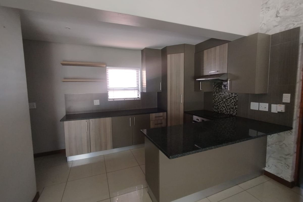 Modern kitchen featuring granite countertops, ample built-in cabinetry, a mosaic tile backsplash, and an integrated extractor fan with tiled flooring throughout.