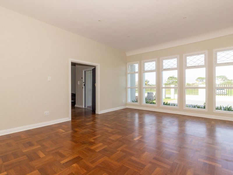 A bright, empty office space featuring polished parquet flooring, large leaded glass windows, and neutral wall finishes.