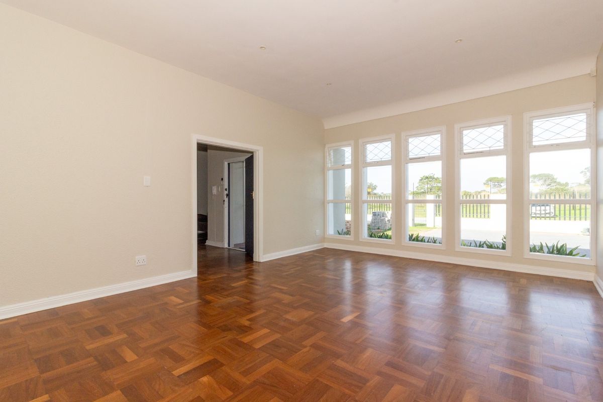 A bright, empty office space featuring polished parquet flooring, large leaded glass windows, and neutral wall finishes.