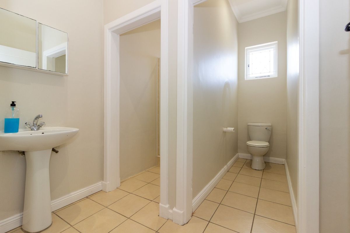 A clean and functional bathroom featuring a pedestal basin, a separate toilet area, and neutral tiled flooring.