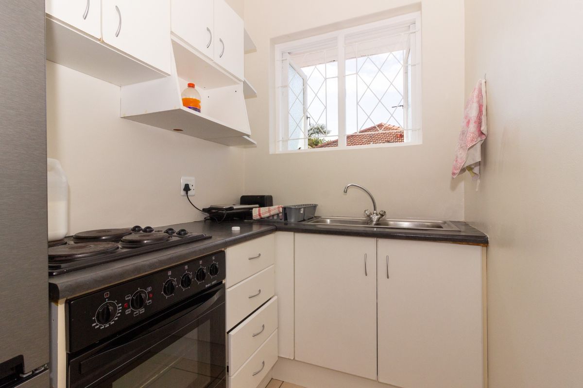 Compact kitchen area featuring white cabinetry, a dark laminate countertop, stainless steel sink, and a built-in electric stove with oven.