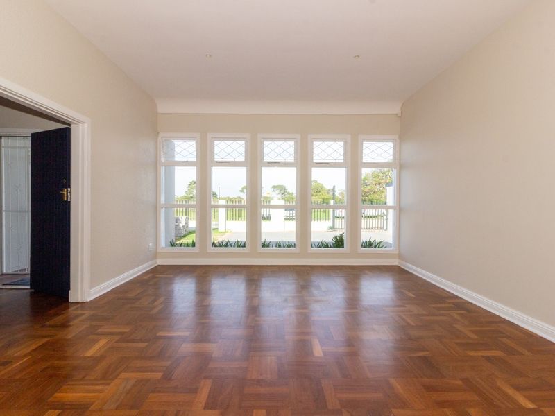 A bright, empty office space featuring polished parquet flooring, neutral walls, and large windows with leaded glass detailing.