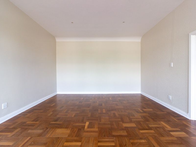 A bright, empty office space featuring well-maintained parquet flooring, neutral walls, and recessed ceiling lighting.