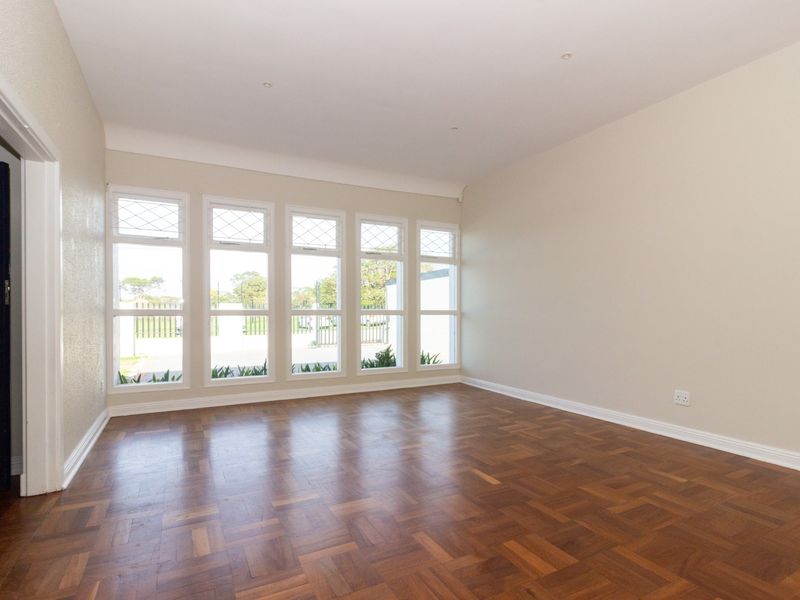 A bright, empty office space featuring polished parquet flooring, neutral walls, and large windows providing ample natural light.