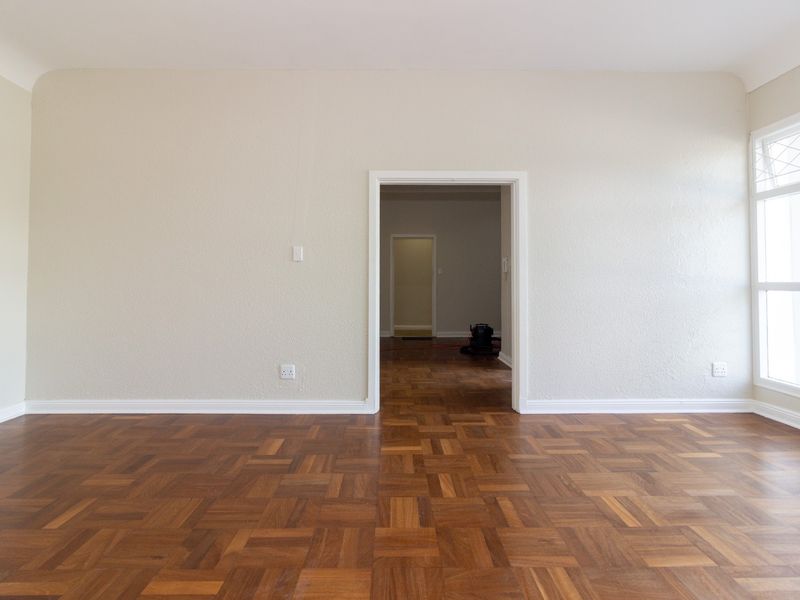 A bright, empty office space featuring well-maintained parquet flooring, neutral walls, and a large window with leaded glass detailing.