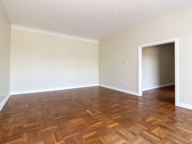 A bright, empty office space featuring well-maintained parquet flooring, neutral walls, and recessed downlighting, offering a clean and professional environment.